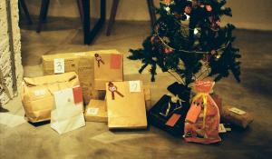 gifts wrapped in brown paper bags and cloth bags under a small christmas tree